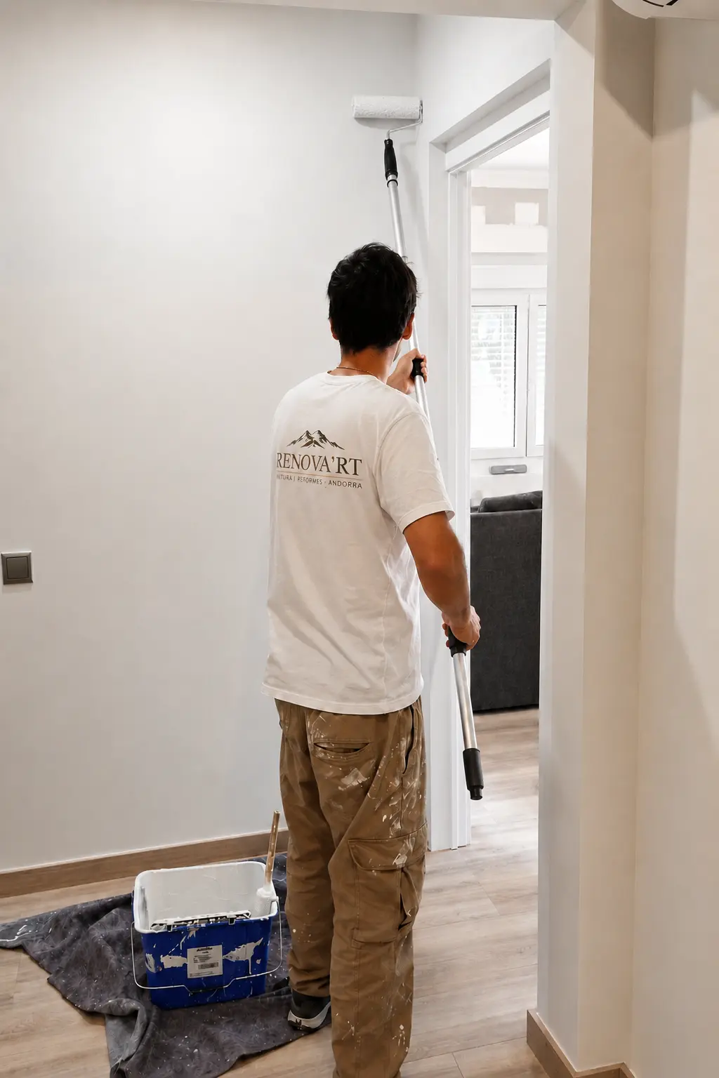 Pintor de Renova'rt amb samarreta corporativa pintant una paret interior blanca amb corró a un habitatge d'Andorra